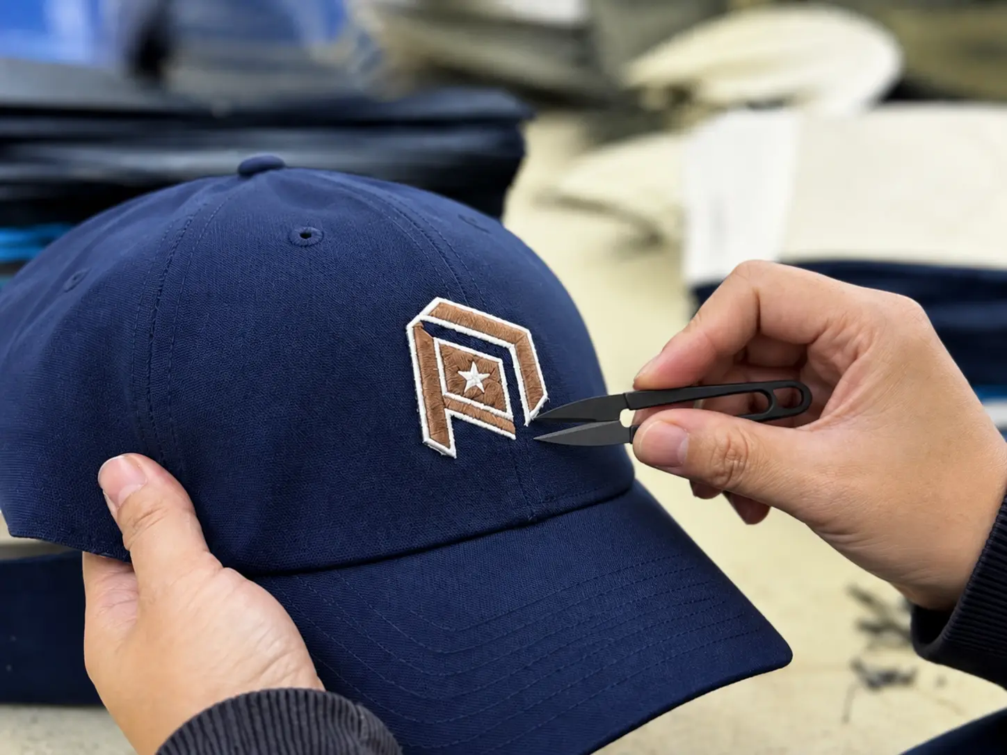Custom hat quality control process with hands trimming embroidery threads and inspecting logo details on a finished cap